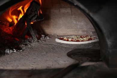 Photo of Burning firewood and tasty pizza in oven at restaurant kitchen