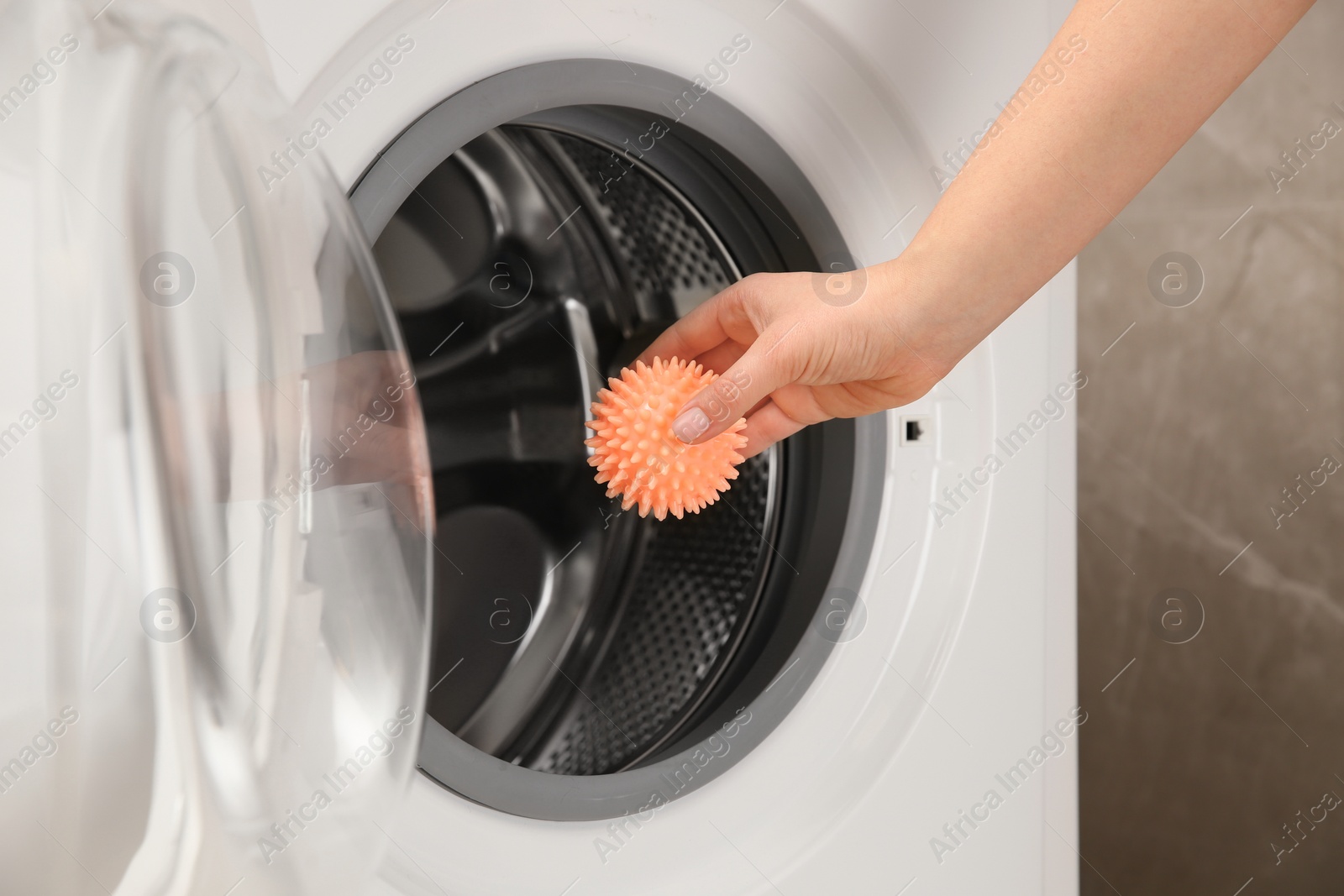 Photo of Woman putting dryer ball into washing machine, closeup