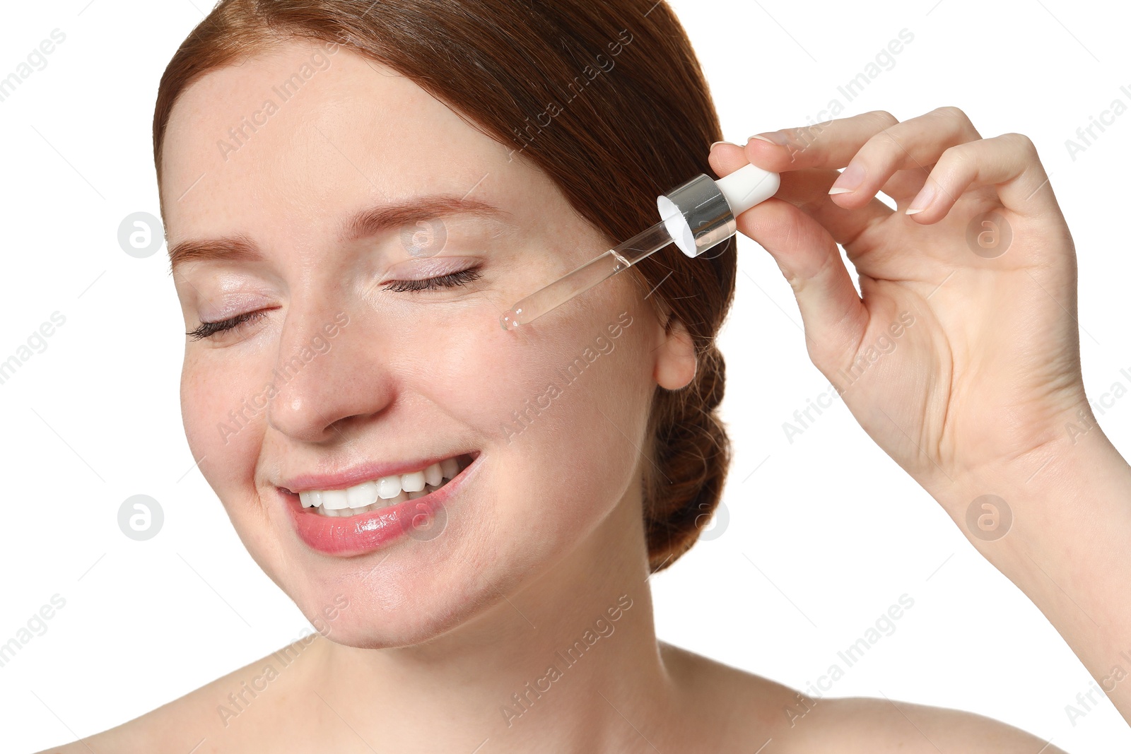 Photo of Smiling woman with freckles applying cosmetic serum onto her face on white background, closeup