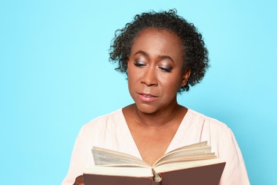 Portrait of mature African-American woman reading book on light blue background