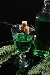 Photo of Absinthe, brown sugar, spoon and green leaves on mirror table. Alcoholic drink