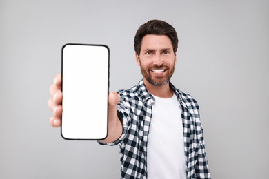 Photo of Handsome man showing smartphone in hand on light grey background