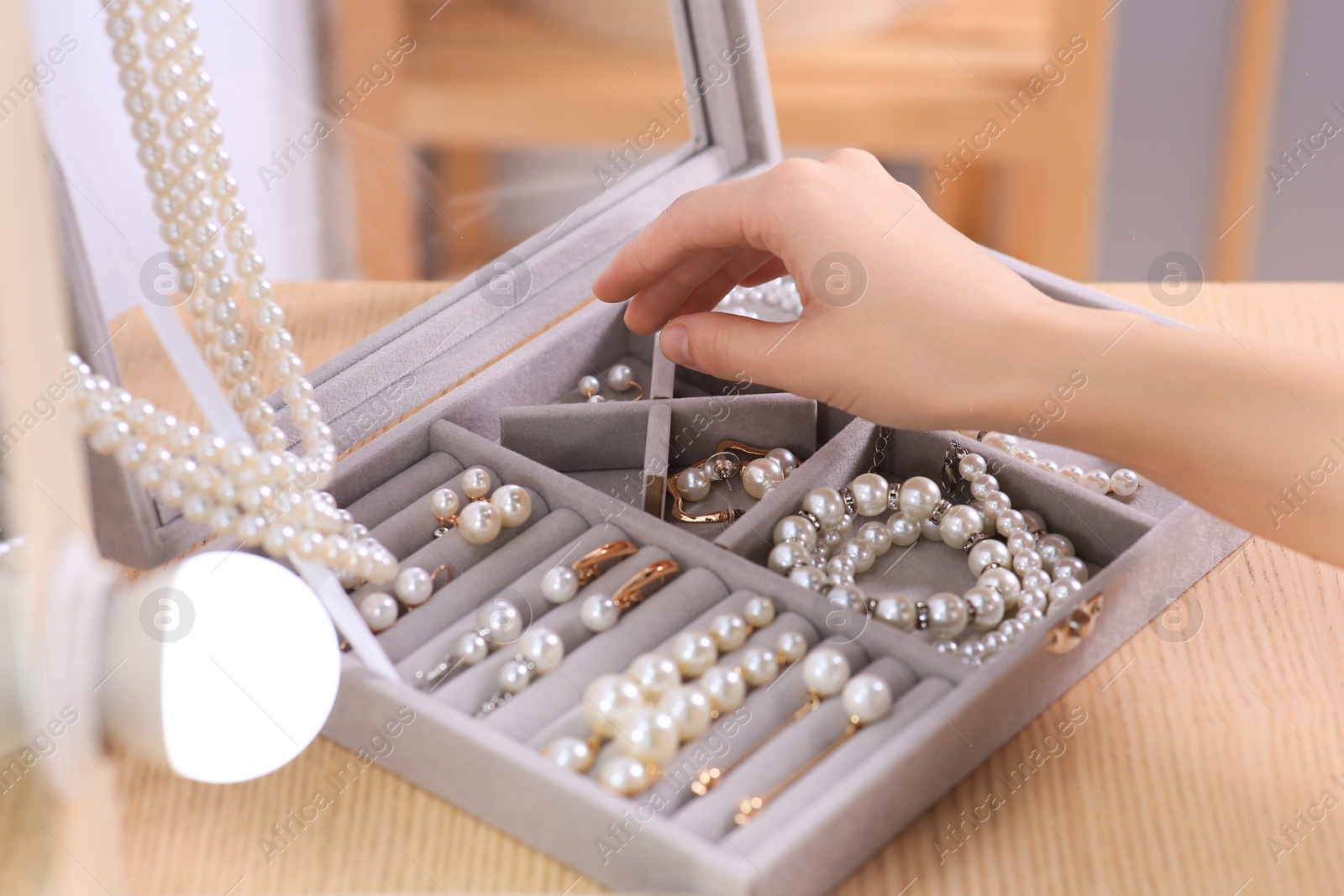 Photo of Young woman taking elegant pearl jewelry at dressing table indoors, closeup