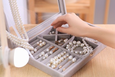 Young woman taking elegant pearl jewelry at dressing table indoors, closeup