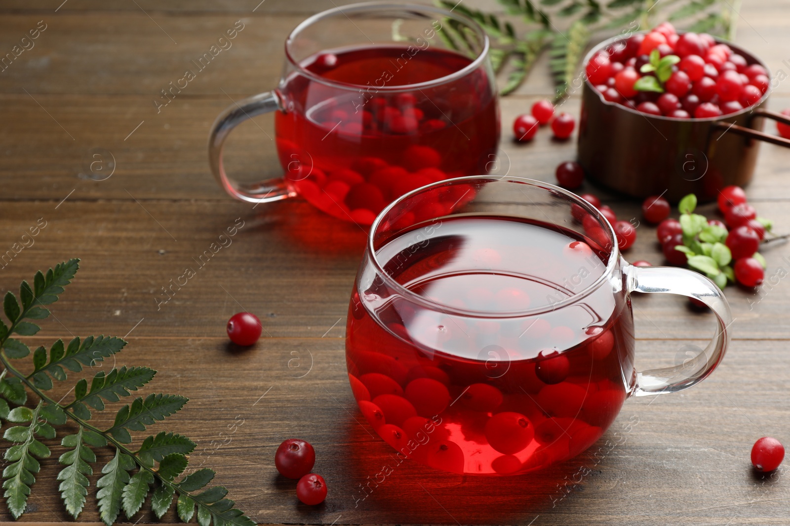 Photo of Tasty hot cranberry tea in glasses and fresh berries on wooden table