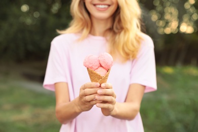 Photo of Happy young woman with delicious ice cream in waffle cone outdoors, closeup