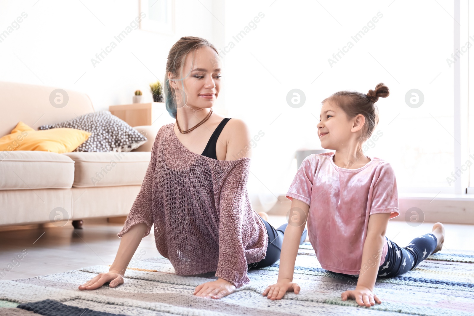 Photo of Young mother and her daughter practicing yoga at home