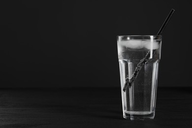 Glass of refreshing soda water with ice cubes and straw on black table, space for text