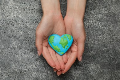 Photo of Happy Earth Day. Woman with heart shaped plasticine planet at grey table, top view