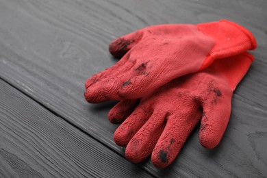 Photo of Pair of red gardening gloves on grey wooden table, closeup. Space for text