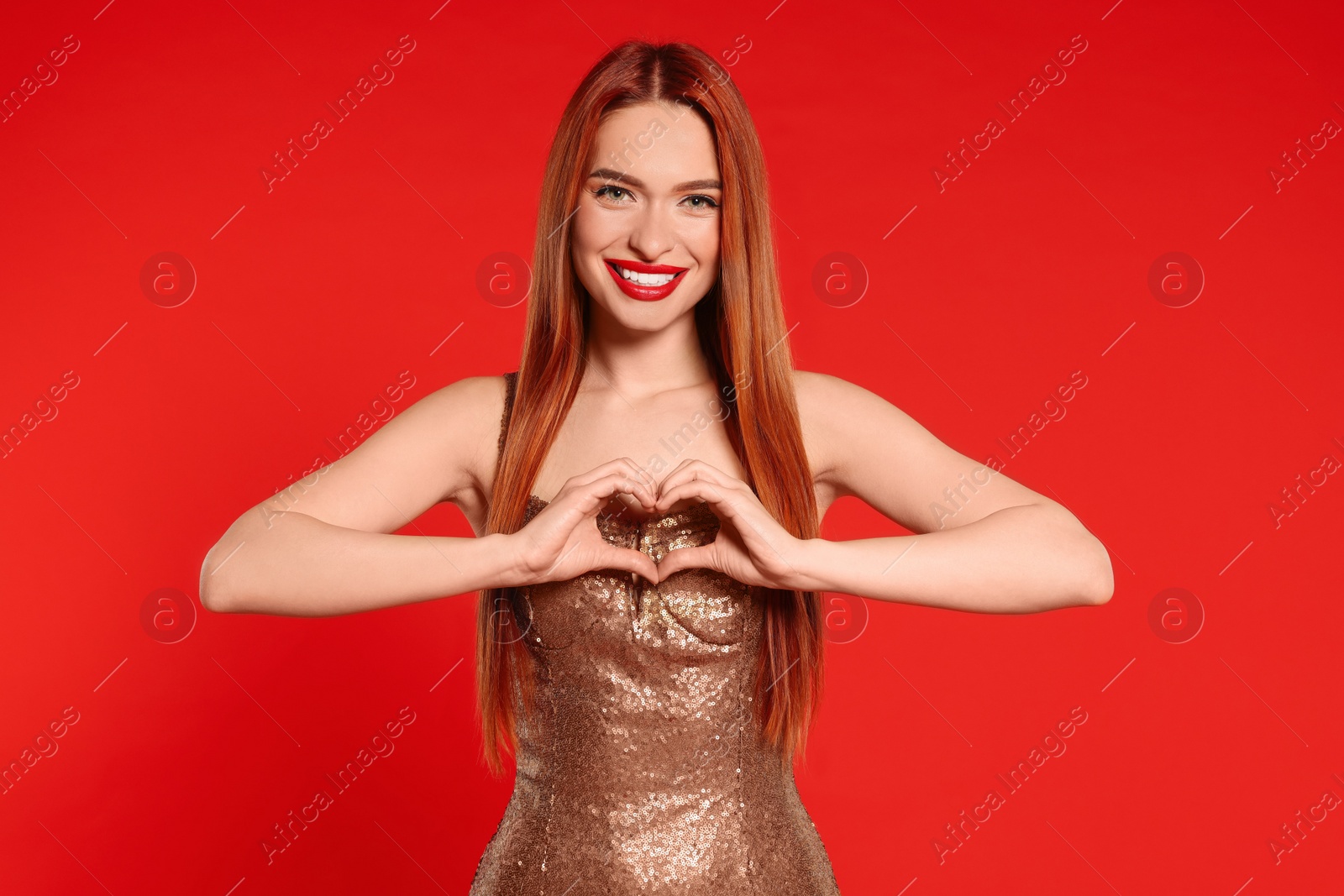 Photo of Young woman in dress making heart with hands on red background