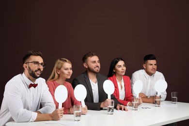 Panel of judges holding blank score signs at table on brown background. Space for text