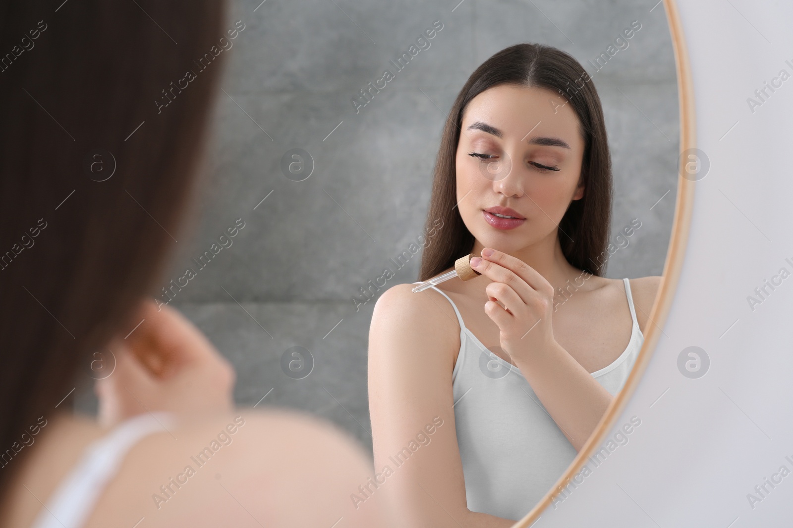 Photo of Woman applying essential oil onto shoulder near mirror