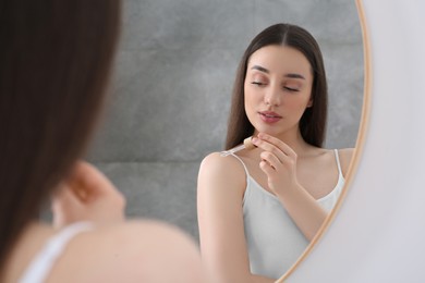 Woman applying essential oil onto shoulder near mirror