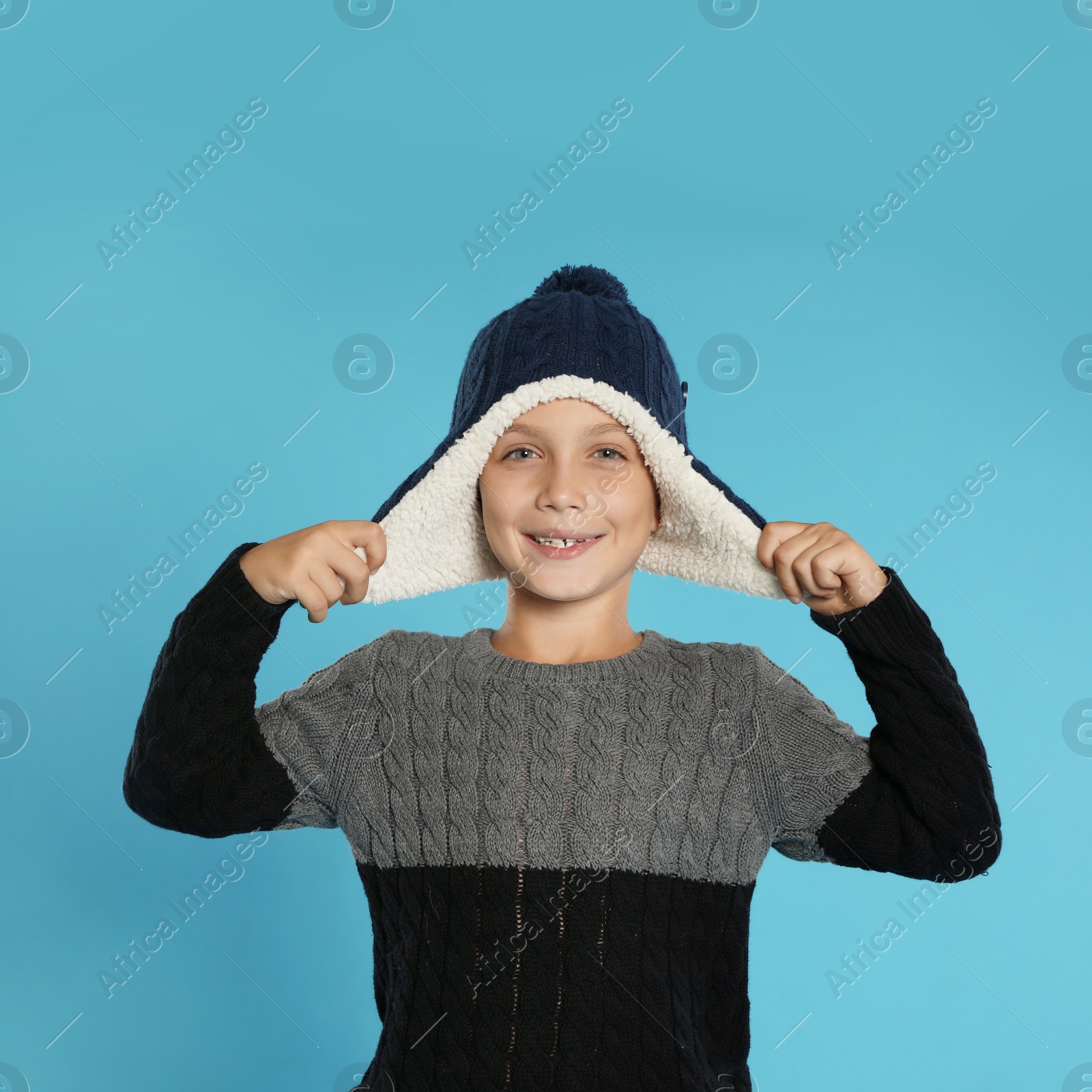 Photo of Cute little boy in sweater and hat on blue background. Winter season