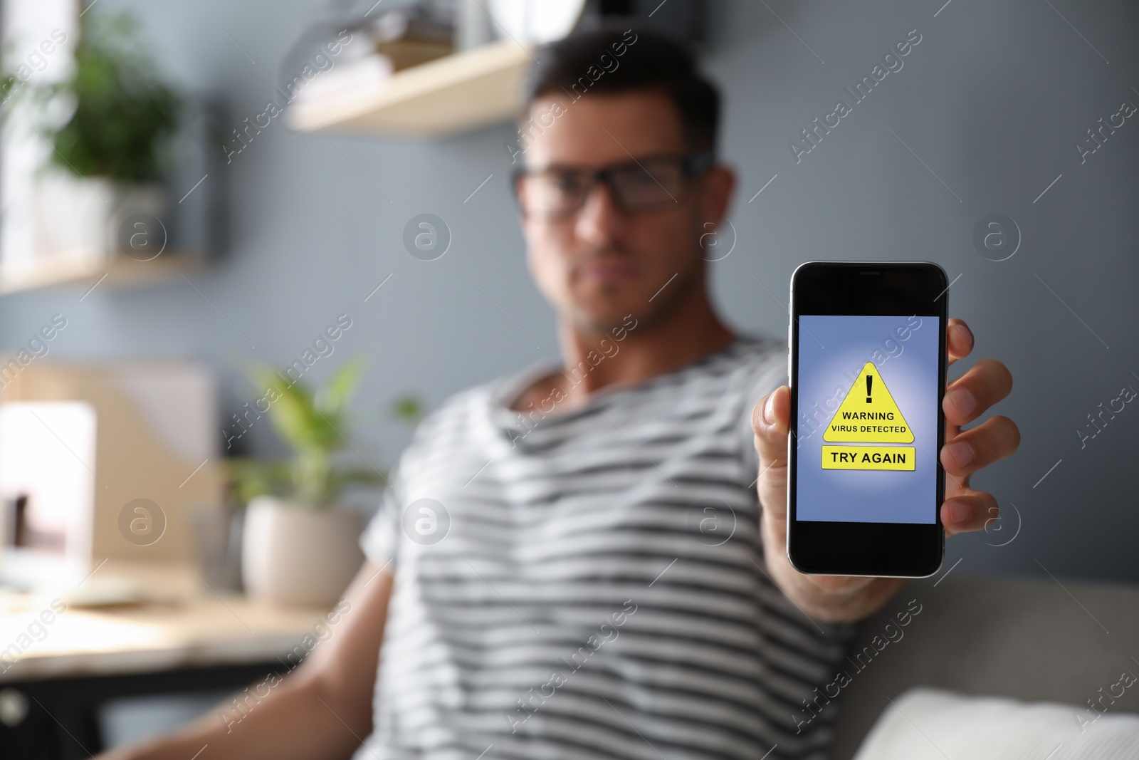 Photo of Man holding smartphone with warning about virus attack at home, focus on hand