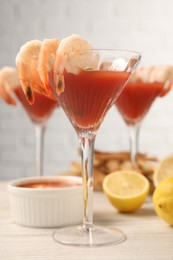 Tasty shrimp cocktail with sauce in glasses and lemon on light wooden table, closeup