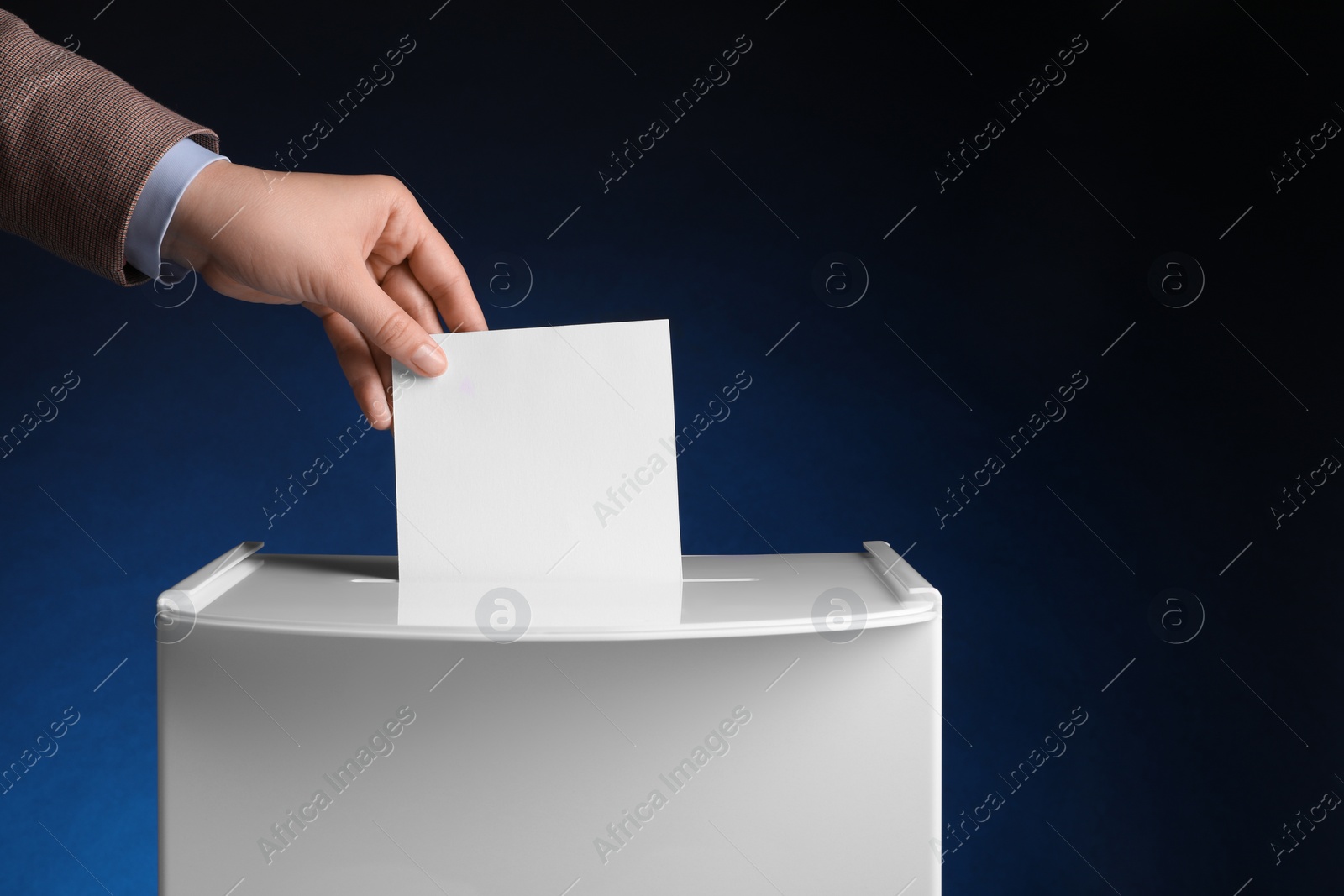 Photo of Woman putting her vote into ballot box on dark blue background, closeup. Space for text