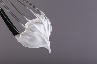 Whisk with whipped cream on grey background, closeup. Space for text