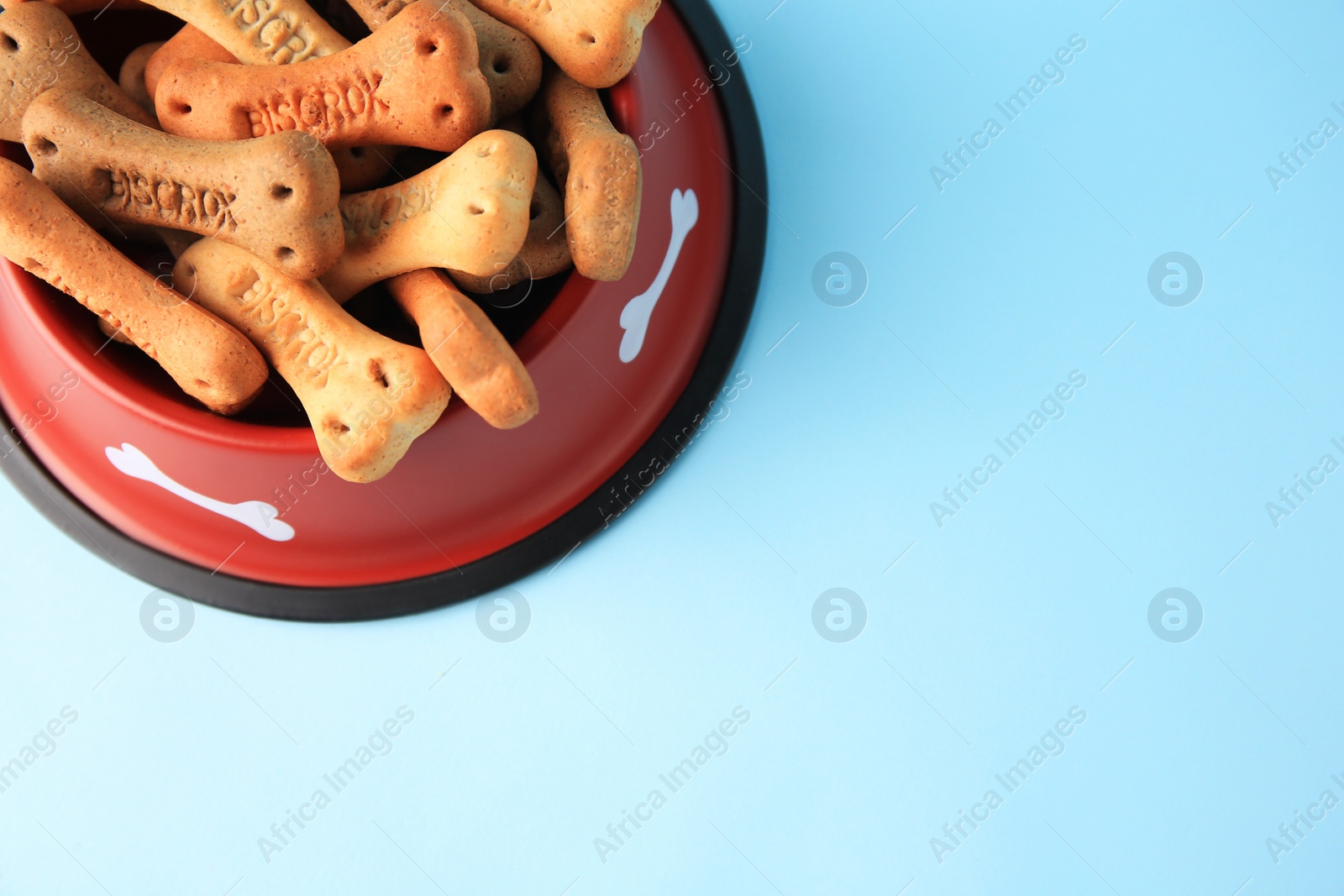 Photo of Bone shaped dog cookies in feeding bowl on light blue background, above view. Space for text