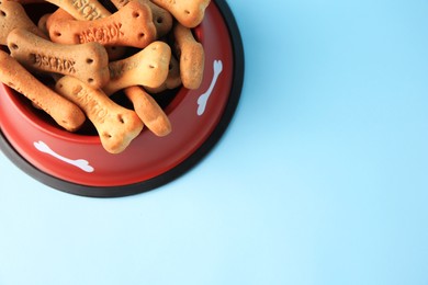 Bone shaped dog cookies in feeding bowl on light blue background, above view. Space for text