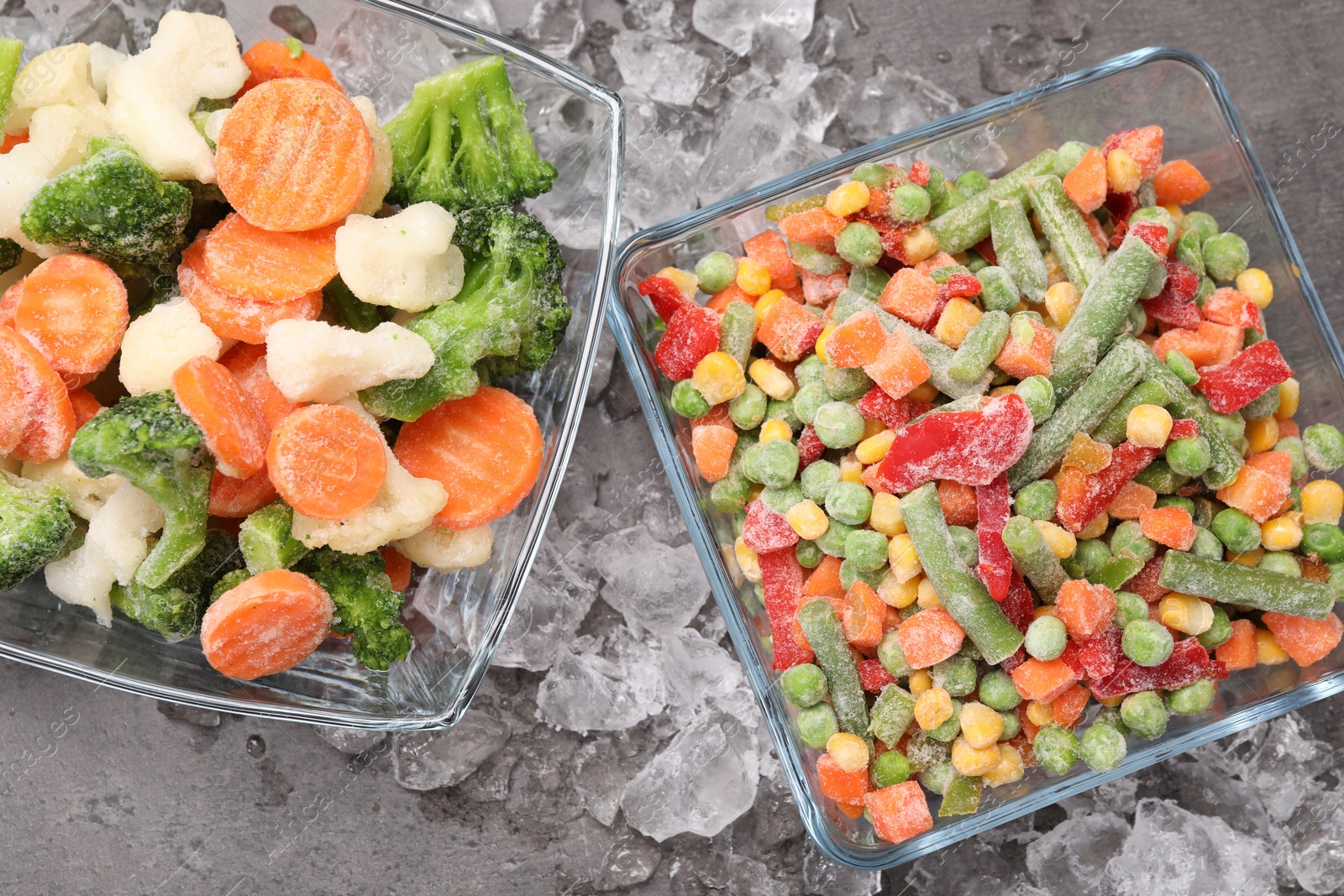 Photo of Mix of different frozen vegetables with ice on grey textured table, flat lay