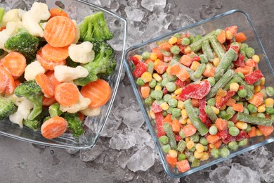 Mix of different frozen vegetables with ice on grey textured table, flat lay