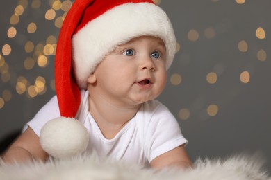 Photo of Cute baby in Santa hat on fluffy carpet against blurred lights. Christmas celebration