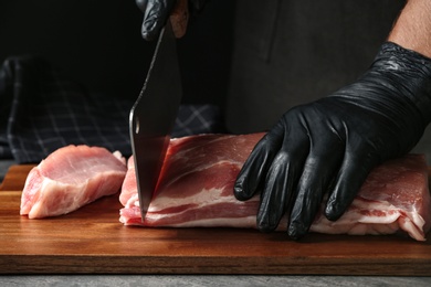 Man cutting fresh raw meat on table against dark background, closeup