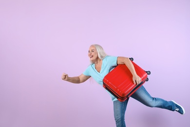 Photo of Senior woman with suitcase running on color background. Vacation travel
