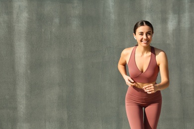 Happy young woman in stylish sports wear running on grey background. Space for text