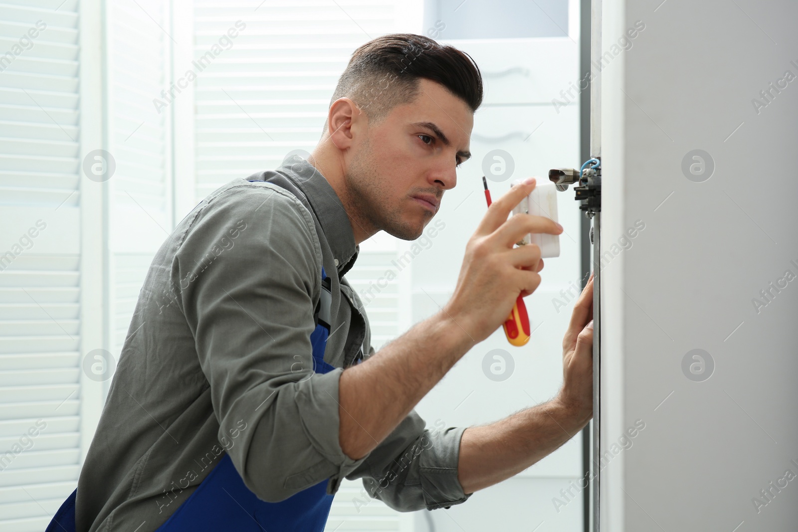 Photo of Professional electrician with screwdriver repairing light switch indoors