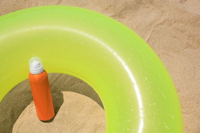 Photo of Sunscreen and inflatable ring on sand, above view. Sun protection care