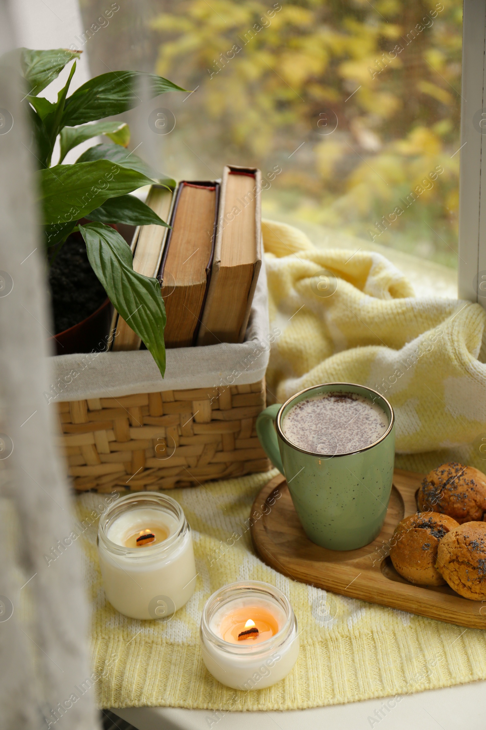 Photo of Burning aromatic candles, cup with hot drink and cookies on windowsill indoors. Autumn coziness