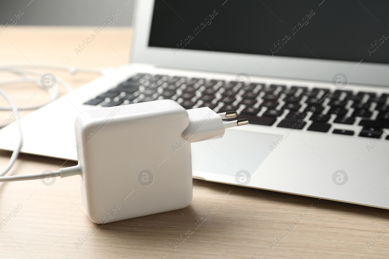 Photo of Charger and laptop on wooden table. Modern technology