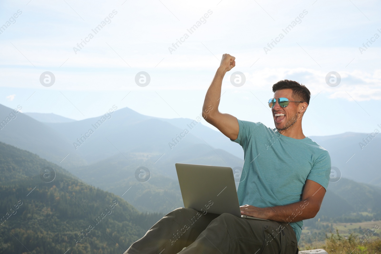 Photo of Man working with laptop in mountains on sunny day