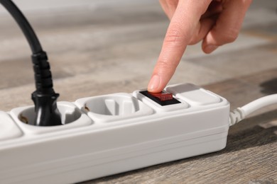 Photo of Man pressing power button of extension board on floor, closeup