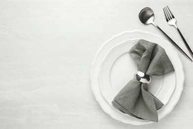 Stylish setting with cutlery, napkin and plates on light textured table, flat lay. Space for text