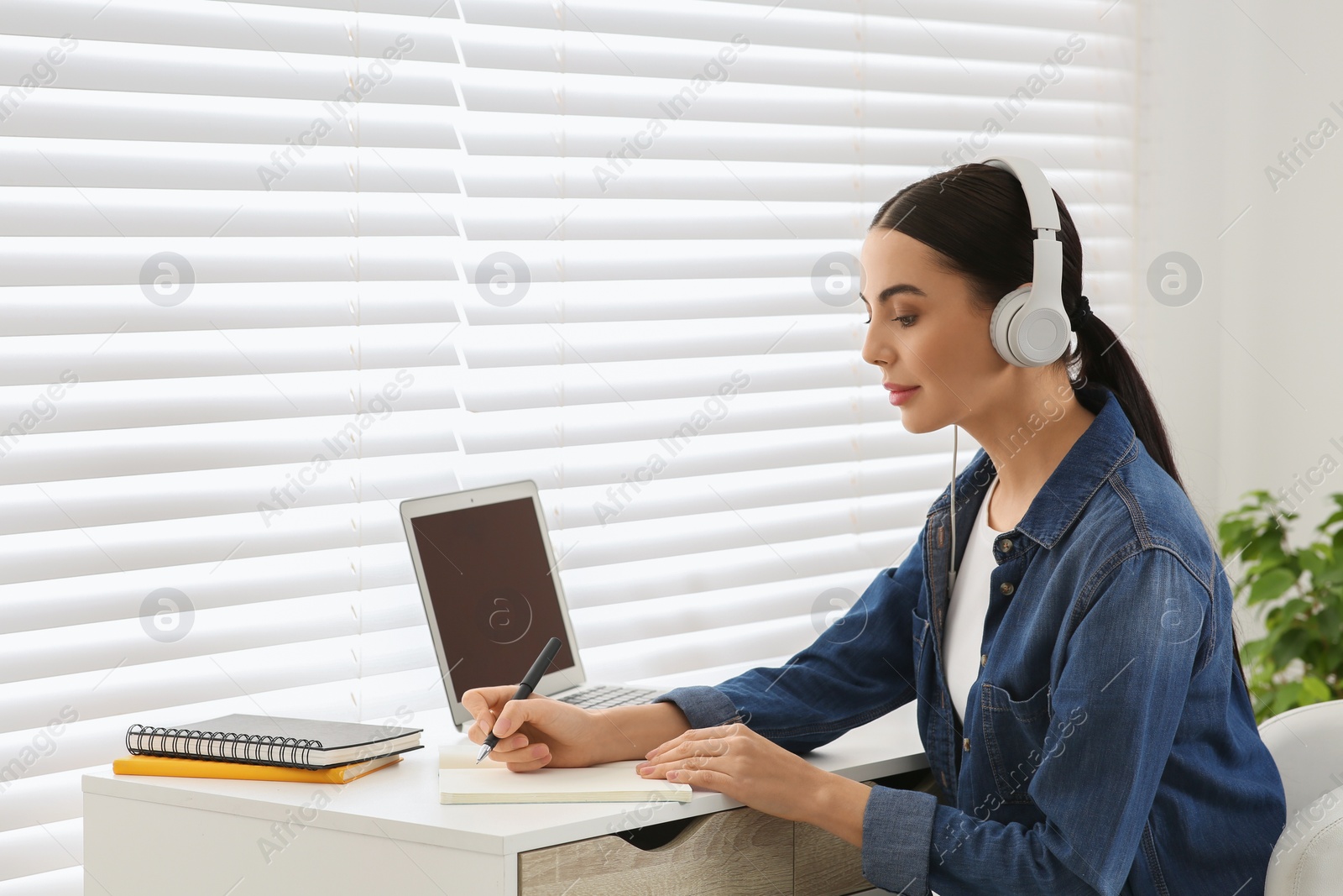 Photo of Online translation course. Student in headphones writing near laptop at home