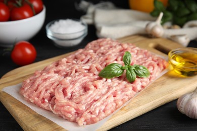 Photo of Raw chicken minced meat with basil on black wooden table, closeup