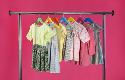 Rack with stylish children clothes on pink background
