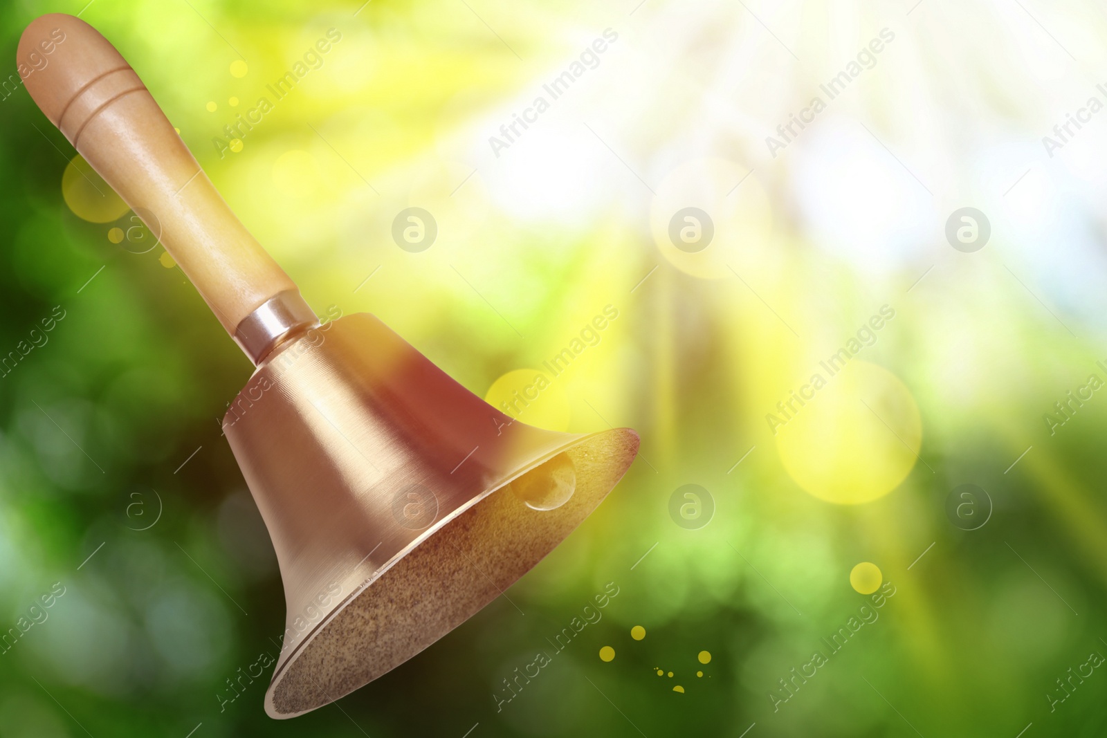 Image of Shiny school bell with wooden handle outdoors, space for text. Bokeh effect