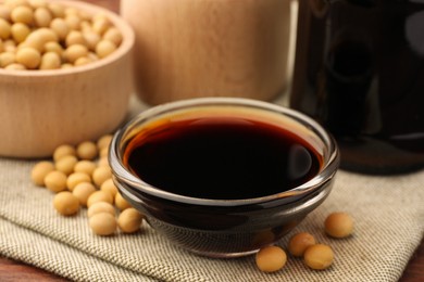 Soy sauce in bowl and soybeans on table, closeup