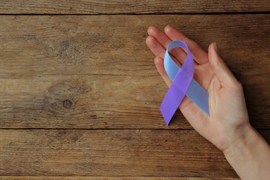 Image of World Arthritis Day. Woman with blue and purple awareness ribbon on wooden background, top view. Space for text