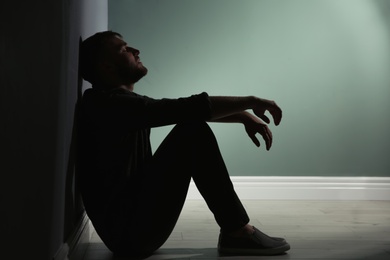 Photo of Depressed young man sitting on floor in darkness