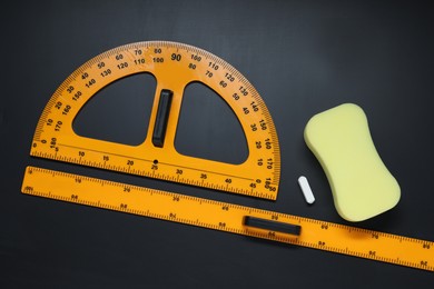 Photo of Ruler, protractor, chalk and sponge on black table, flat lay