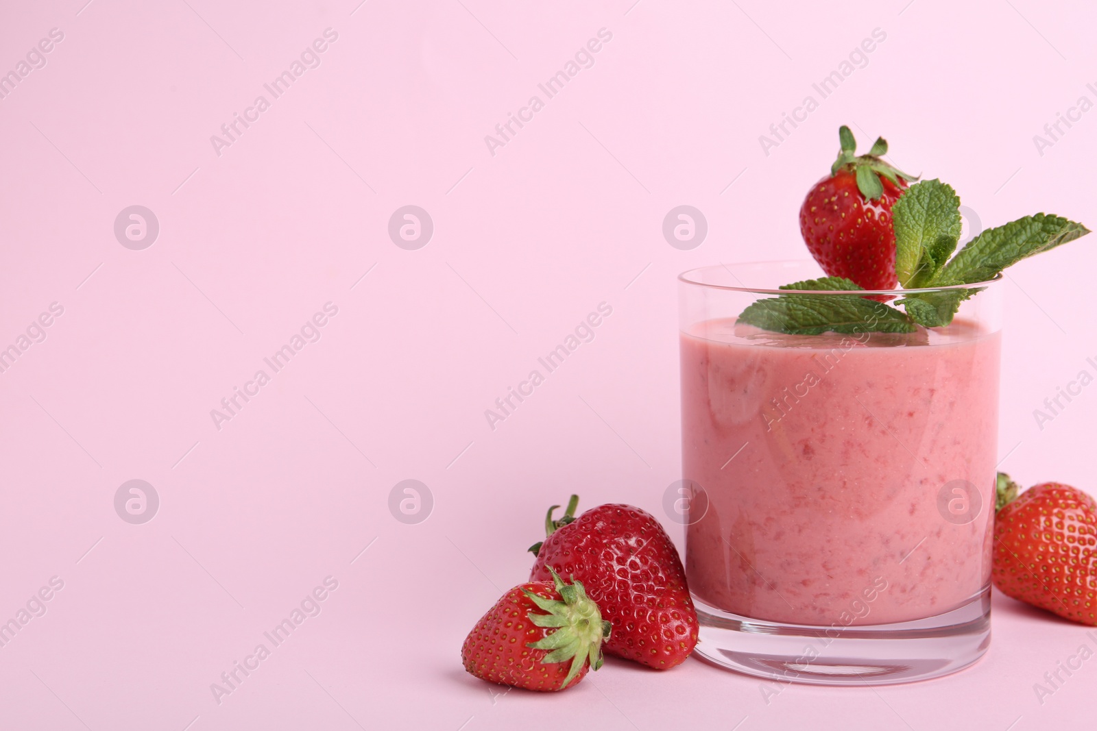 Photo of Tasty strawberry smoothie with mint in glass on pink background. Space for text