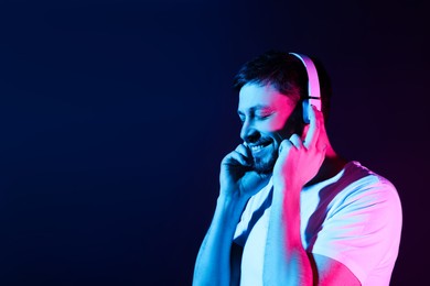 Photo of Handsome man in headphones enjoying music in neon lights against dark blue background. Space for text
