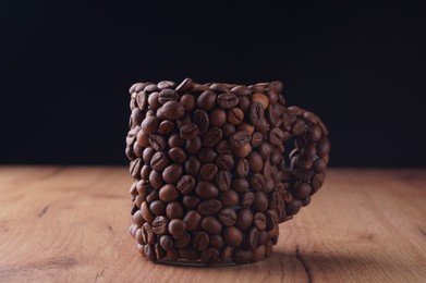 Photo of Cup made of coffee beans on wooden table against black background