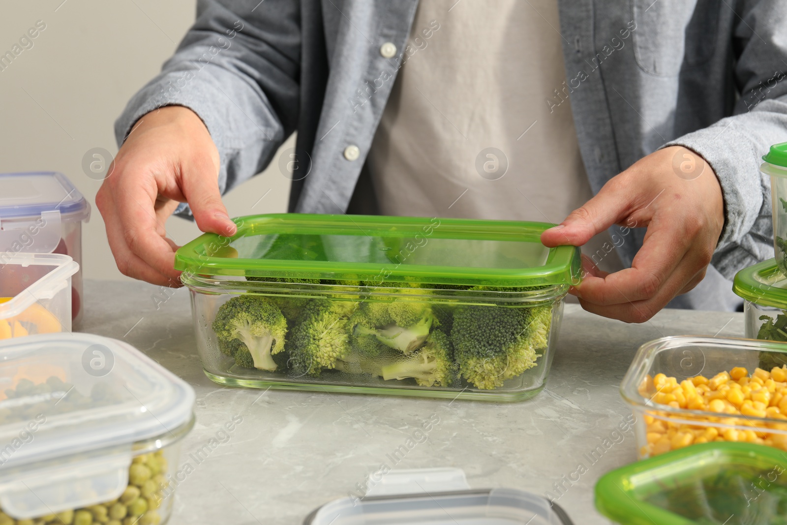 Photo of Man closing glass container with lid at light grey marble table in kitchen, closeup. Food storage